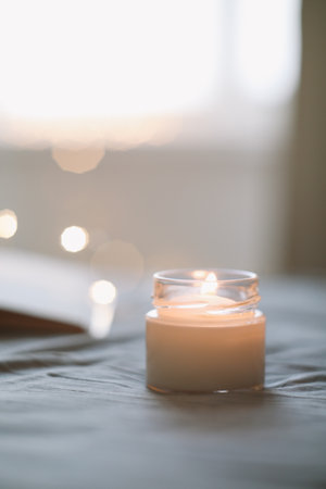 Cozy still life composition with a scented burning candle in glass jar in bed close up. Good morning. Cozy homeの写真素材