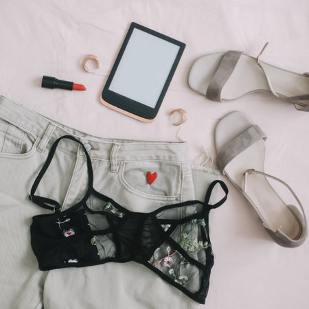 Overhead view of womans casual spring outfit with phone or tablet, jeans, sandals, underwear, red lipstick and earrings on beige background, Flat lay, top viewの写真素材