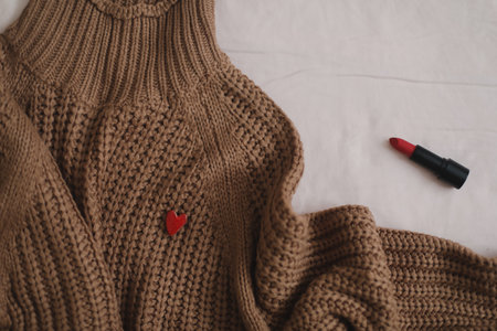 Overhead view of womans casual outfit with warm knitted sweater, red lipstick and earrings on beige background in bed, Flat lay, top viewの写真素材