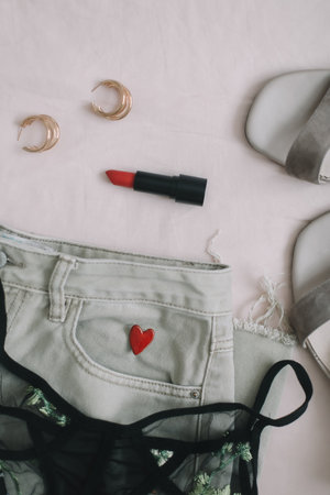 Overhead view of womans casual spring outfit with phone or tablet, jeans, sandals, underwear, red lipstick and earrings on beige background, Flat lay, top viewの写真素材