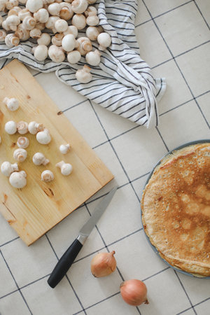 fresh whole and sliced champignon mushrooms and knife on wooden board. Cooking pancakes with mushrooms on a white table top viewの写真素材