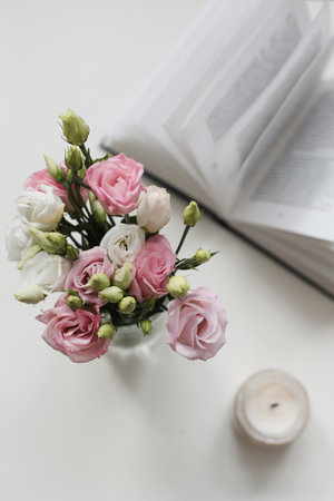 Home decoration and interior. Beautiful burning candle with flowers and book on white table. Details of still life in the home interior of living room. Cozy spring concept.の写真素材