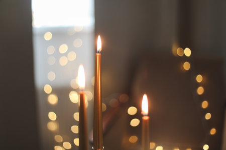Beautiful composition with burning wax candles on table. Elegant golden candlesticks with burning candles in a cozy room interiorの写真素材