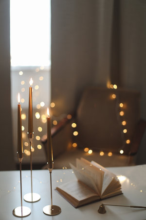 Still life details of home interior, concept of coziness and home atmosphere. beautiful golden candlesticks, scented candle, open book, garland lights. Home autumn concept, Living roomの写真素材