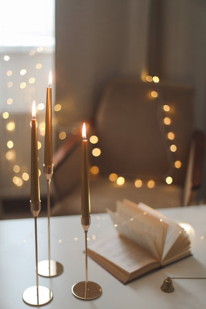 Still life details of home interior, concept of coziness and home atmosphere. beautiful golden candlesticks, scented candle, open book, garland lights. Home autumn concept, Living roomの写真素材