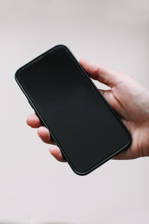 Close up of woman hand using smartphone isolated on white wall. Female hand showing empty screen of modern smart phone. Hand holding black smartphone isolated on white background, clipping pathの写真素材