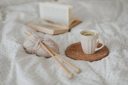 Cozy morning still life with a coffee cup, candle, needles and a woolen yarn in white bed. Knitting warm woolen sweater or scarf top view. Hygge lifestyle, cozy mood. Handicraft day concept.の写真素材