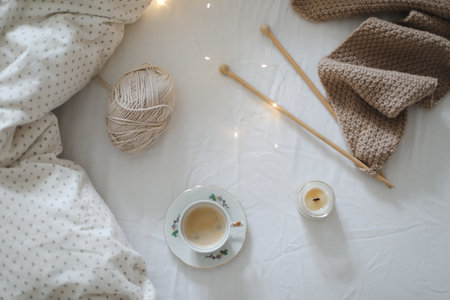 Cozy morning still life with a coffee cup, candle, needles and a woolen yarn in white bed. Knitting warm woolen sweater or scarf top view. Hygge lifestyle, cozy mood. Handicraft day concept.の写真素材