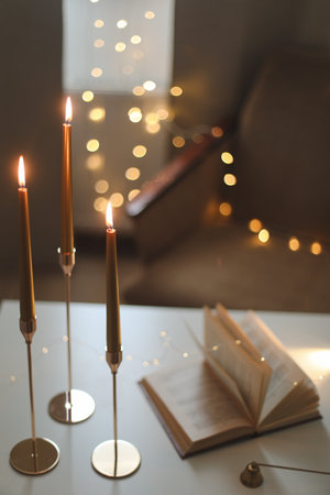 Still life details of home interior, concept of coziness and home atmosphere. beautiful golden candlesticks, scented candle, open book, garland lights. Home autumn concept, Living roomの写真素材