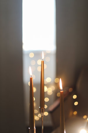 Beautiful composition with burning wax candles on table. Elegant golden candlesticks with burning candles in a cozy room interiorの写真素材