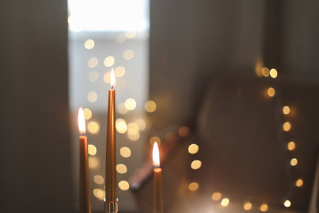 Beautiful composition with burning wax candles on table. Elegant golden candlesticks with burning candles in a cozy room interiorの写真素材