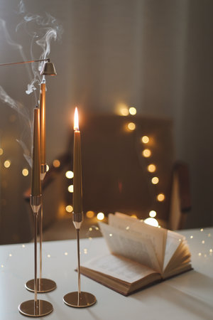 Still life details of home interior, concept of coziness and home atmosphere. beautiful golden candlesticks, scented candle, open book, garland lights. Home autumn concept, Living roomの写真素材