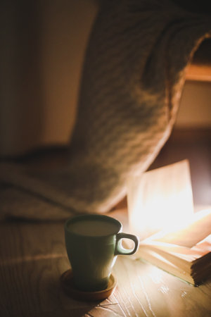 Cozy warm aesthetic evening atmosphere with an open book and plaid, soft focus.の写真素材