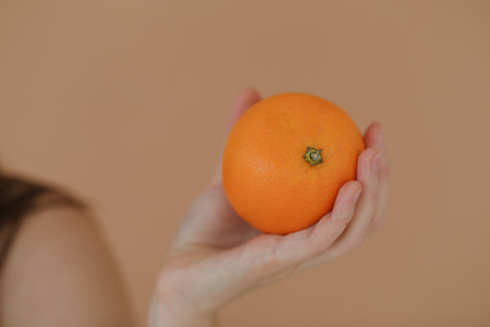 hand holds a fresh tropical orange. An orange in a womans hand on a yellow background isolated. Girl holding a citrus in one handの写真素材