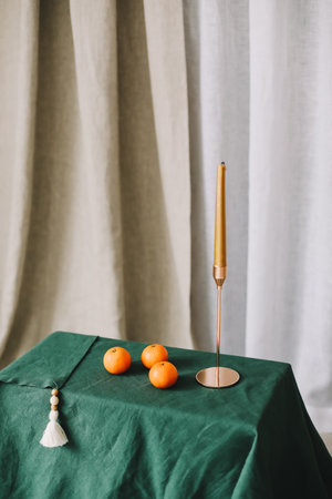 Stylish home decor in rustic style. Table with a golden candle in candlestick, green tablecloth, tangerines. Festive Cozy room decorated for Christmas or New year.の写真素材