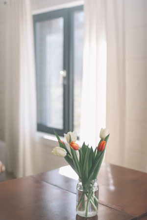 Bouquet of beautiful fresh tulips in a glass vase on wooden table in cozy modern interior. Spring flowers in glass vase at home.の写真素材