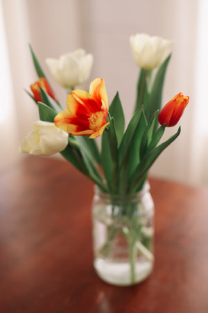 Bouquet of beautiful fresh tulips in a glass vase on wooden table in cozy modern interior. Spring flowers in glass vase at home.の写真素材