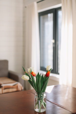 Bouquet of beautiful fresh tulips in a glass vase on wooden table in cozy modern interior. Spring flowers in glass vase at home.の写真素材
