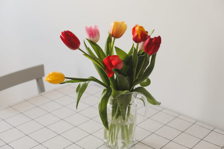 Fresh spring colorful bouquet of tulips in vase standing on white table in light classic design...