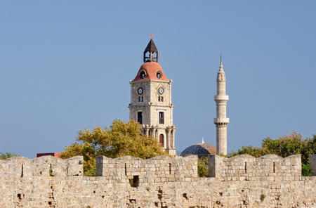 The clock tower and minaret behind the wall of a medieval castle on the island of Rhodesのeditorial素材