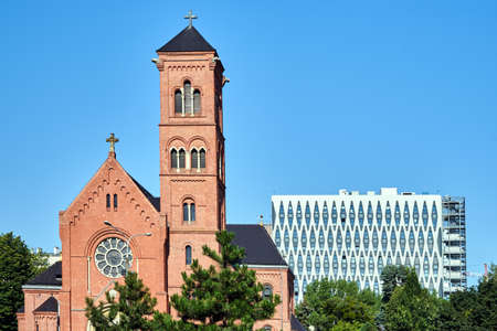 A historic Catholic church with a bell tower and a facade of a modern office building in Poznan