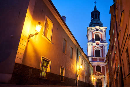 narrow street and belfry of the baroque historic church at night in Poznanの写真素材