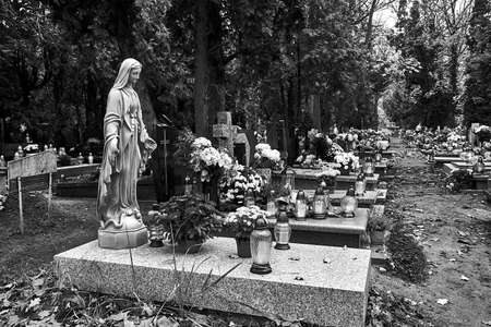 Statue, candles and flowers on graves in a cemetery in Poland, monochromeの写真素材