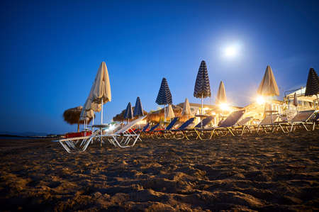 sun loungers and umbrellas on the beach under the moonlight on Crete island, Greeceの写真素材