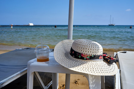 straw hat, mug with cold drink and sunbathing bed on the sandy beach on the island of Crete, Greeceの写真素材