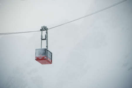 Red funcular cabin covered with snow is moving down in front of the foggy mountain, Alps, Franceのeditorial素材