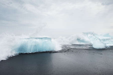 White waves hitting clear blue blocks on the black sand beach, Iceland