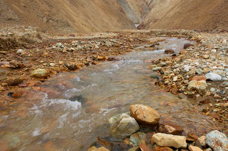 Clear river running among lifeless orange and yellow rocks in Iceland
