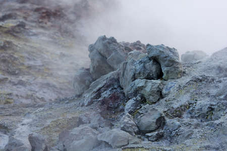 White toxic steam raising behind big colored rock in geothermal area, Iceland