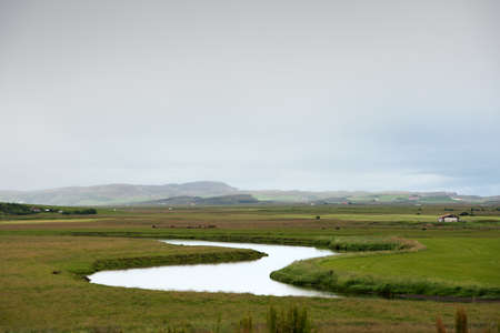 Still river among green hills on a cloudy evening in Icelandの写真素材