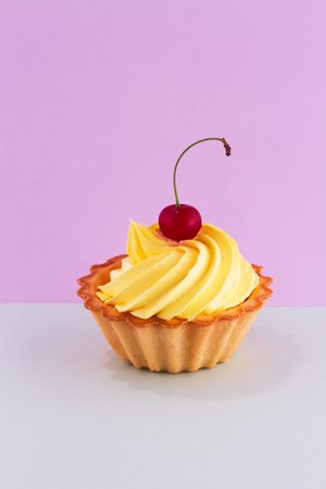 A bright ripe cherry berry on the top of a delicious cake on a double pastel purple-turquoise background.の写真素材