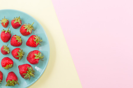 Bright ripe juicy strawberry on a pastel turquoise plate on a double pastel pinkish yellow background.の写真素材