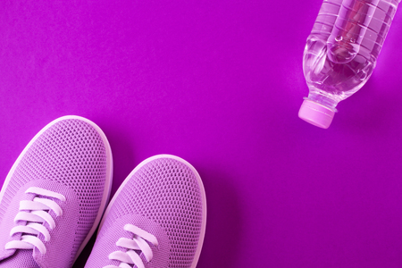 Layout on a bright violet background - light purple sneakers and a bottle of water on a purple background with a place for an inscription.の写真素材