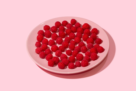 Bright ripe juicy raspberries on a pastel pink plate on a pastel light pink background.の写真素材