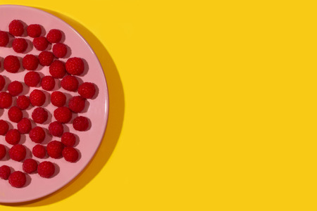 Bright ripe juicy raspberries on a pastel pink plate on a bright yellow background.の写真素材