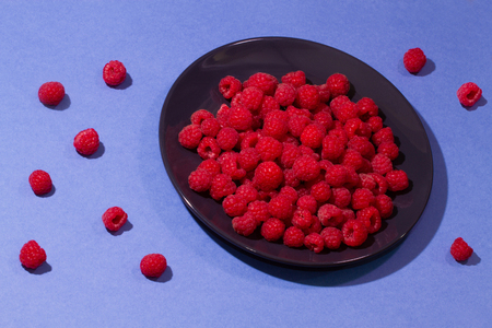 Bright ripe juicy raspberries on a pastel black plate on a pastel blue background.の写真素材