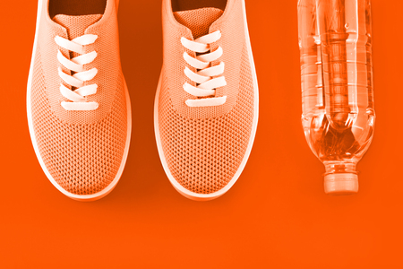 Layout on a bright orange background - light orange sneakers and a bottle of water on a orange background with a place for an inscription.の写真素材