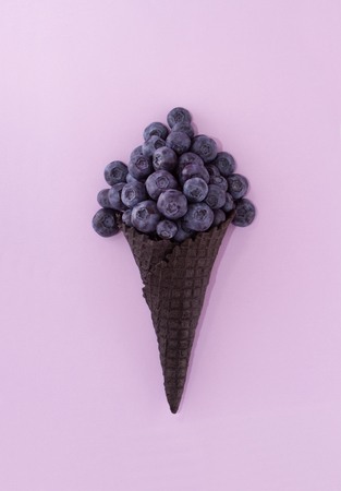 Conceptual art. Blueberry in an ice cream cone on a table on a pastel light purple background. Minimal surrealism.の写真素材