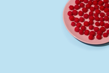 Bright ripe juicy raspberries on a pastel pink plate on a pastel light blue background.の写真素材