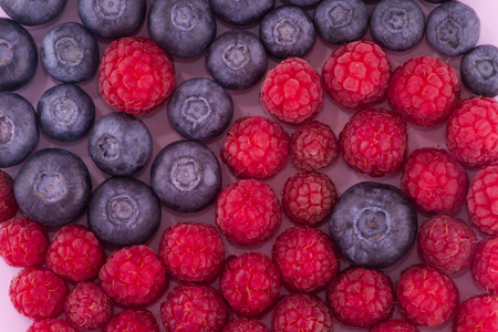 A group of blueberries and raspberries spread out as a Yin-Yang symbol on a light purple background. Can serve as an illustration of the topic of healthy eating.の写真素材