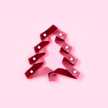 Conceptual photo of a red velvet ribbon with pearl beads in the form of a Christmas tree on a pink paper background with the place for an inscription.の写真素材