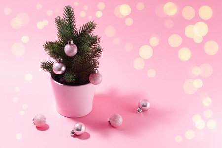 Pale pink composition on a New Year's theme. A small decorative Christmas tree with balls for decoration on a pink background and magical holiday lights.の写真素材