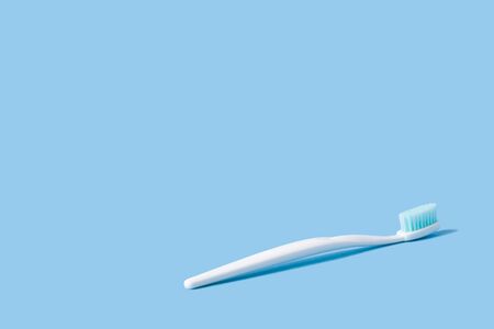 White toothbrush with blue bristles on a pink paper background decorated with spring flowers.の写真素材