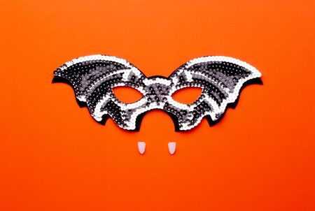 Conceptual halloween flat lay on a bright orange background. Black bat-mask with shiny sequins and...