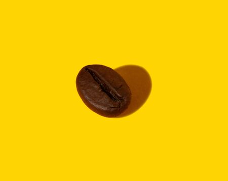 Creative composition of a real closeup macro photography of a coffee bean with a hard shadow in the shape of a heart.の写真素材