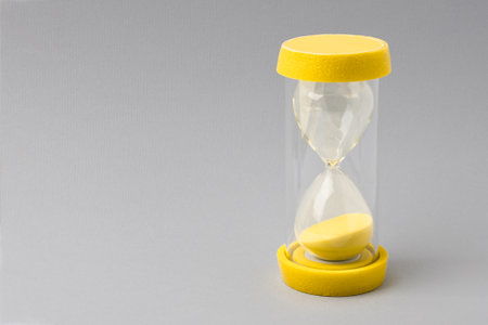 Yellow hourglass on gray paper background.の写真素材